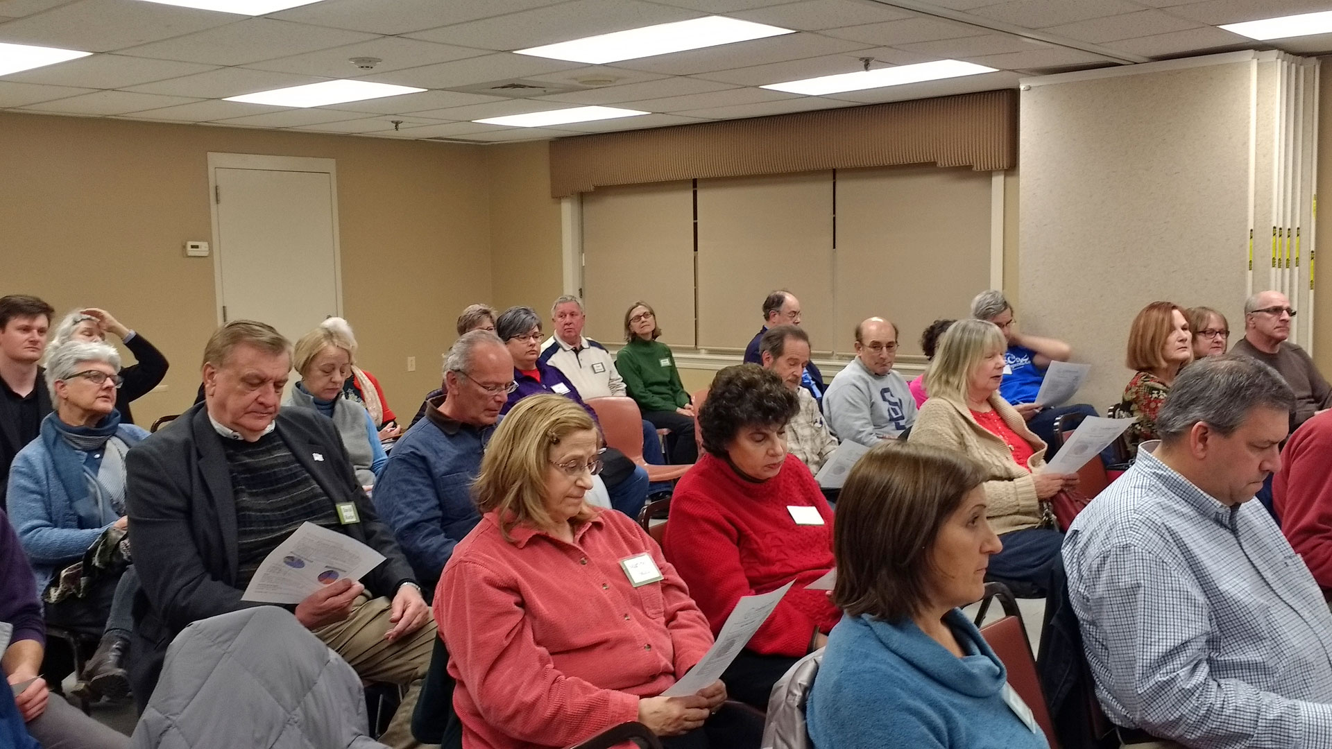 a group of people reading pamphlets at a community meeting