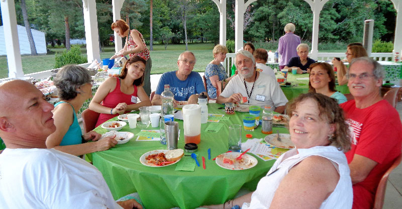 a group of people eating at a table outside and smiling for the camera